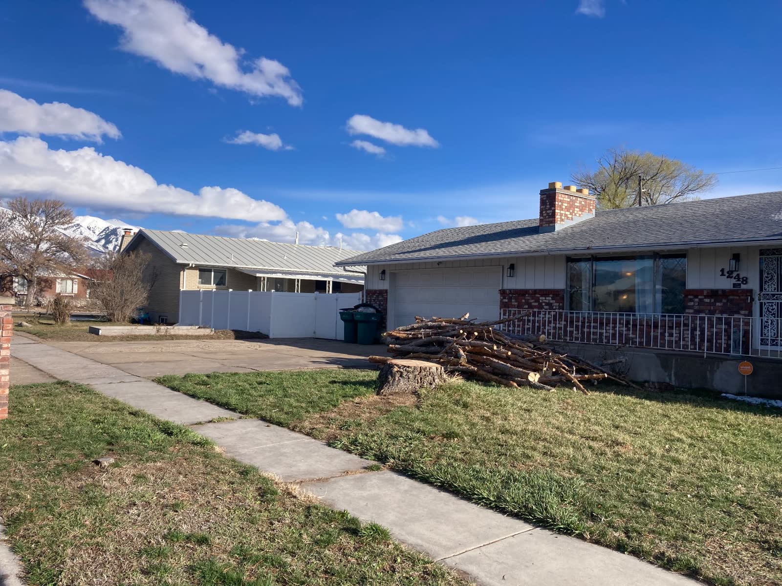 Same front yard cleaned up after storm tree removal, wood stacked neatly by the house
